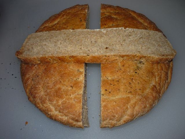 Bread with a slice cut out, laying across the two halves, showing a thin, light crust and normal crumb texture.